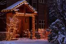 Christmas lights wrapping a houses entrance way with snow on the ground