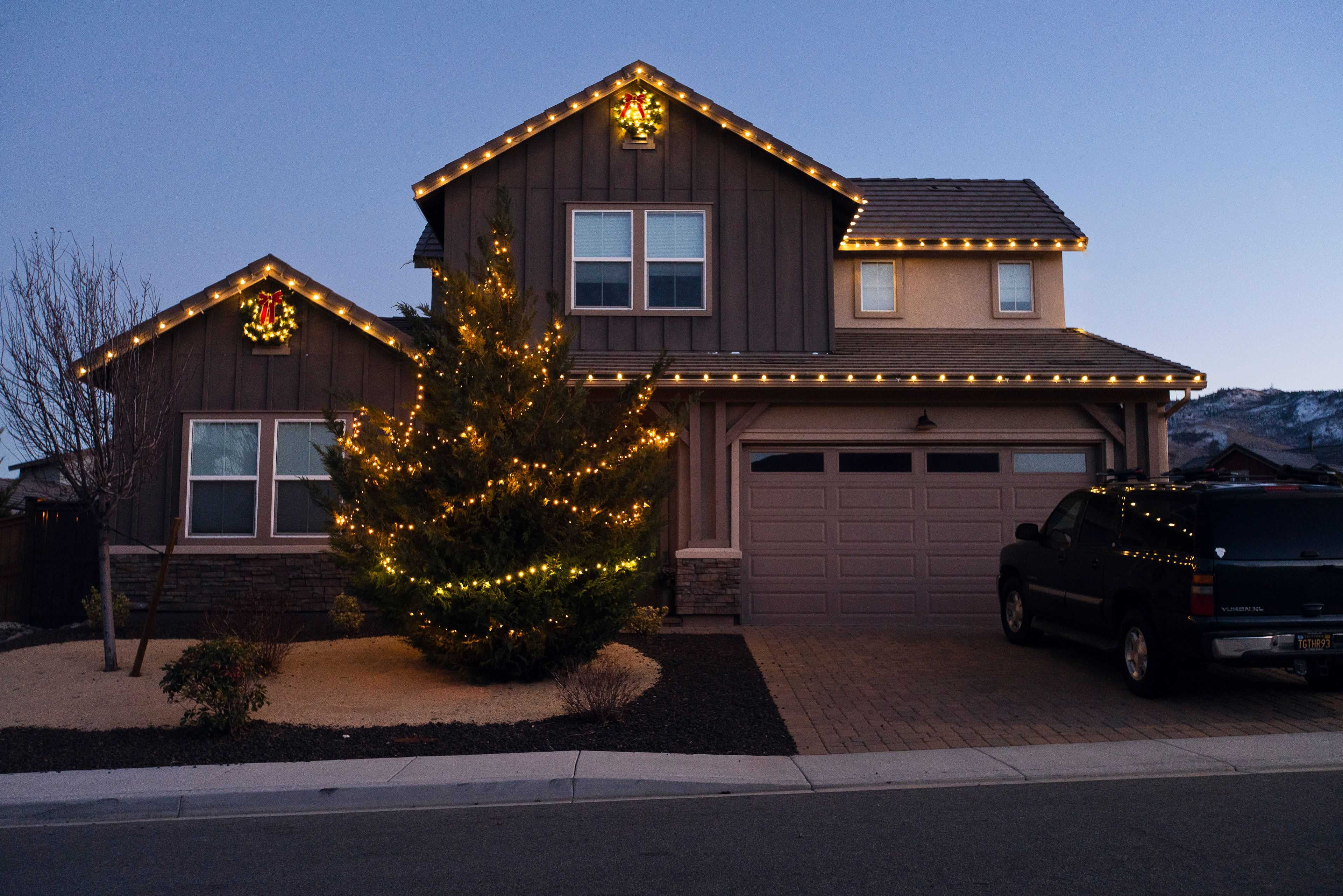 a residential two story home with christmas lights and two wreaths with a lit tree in the front yard