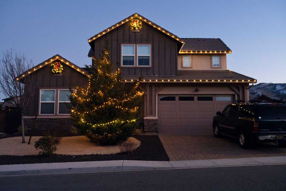 a residential two story home with christmas lights and two wreaths with a lit tree in the front yard