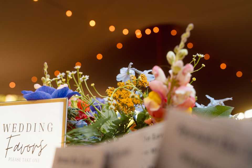 tent lighting behind flowers at the wedding favors table