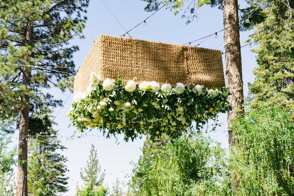 flowers in rattan box hanging upside down above an outdoor wedding dance floor